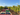 Tractor harvesting grapes in a vineyard with rows of green and red bins filled with grapes.