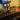Wine bottle and two glasses on a wooden surface with a TV in the background.