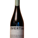 A dark glass wine bottle with a pale green capsule and a white label reading 'OVERTIME' stands on a wooden surface against a wooden background.