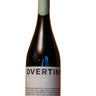 A dark glass wine bottle with a pale green capsule and a white label reading 'OVERTIME' stands on a wooden surface against a wooden background.